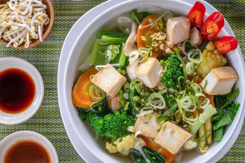 Vietnamese vegetarian noodle soup Pho served in white round bowl with sauces lime chili and bean sprouts