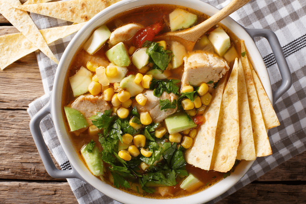 spicy tortilla soup with chicken cilantro tomatoes avocado and corn close up on the table horizontal top view from above