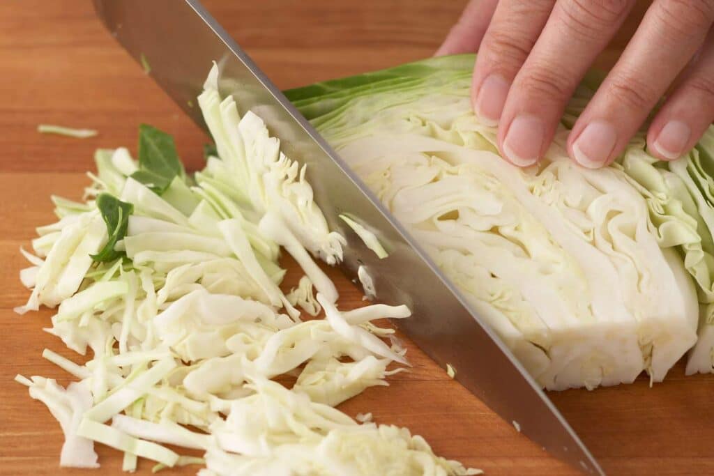 A person chopping cabbage with a knife