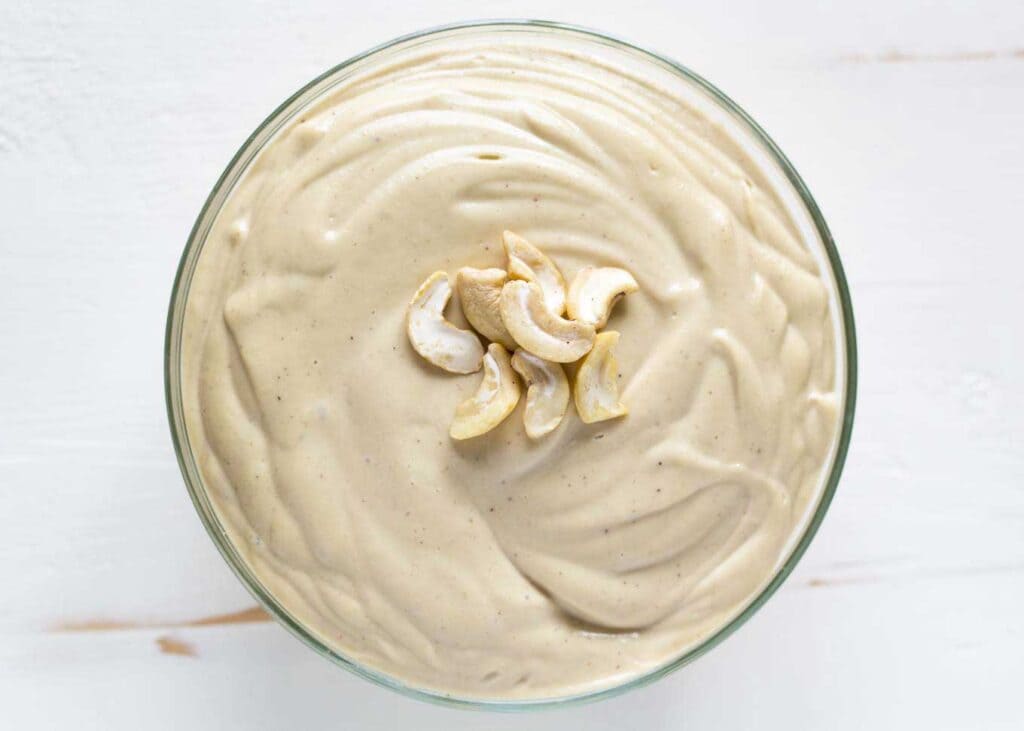 A top view of a cashew cream in a blender topped with cashew nuts