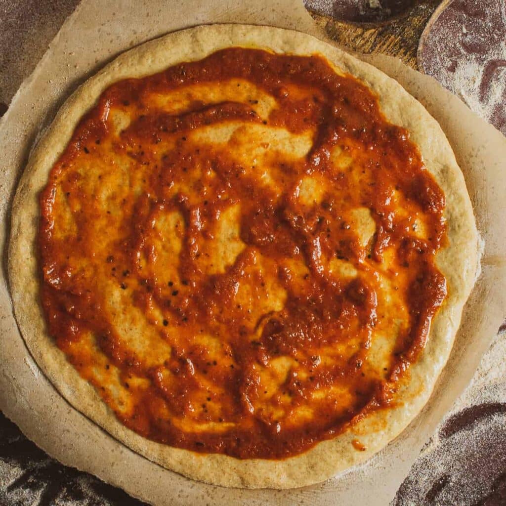 A top view of a pizza dough with tomato sauce on it