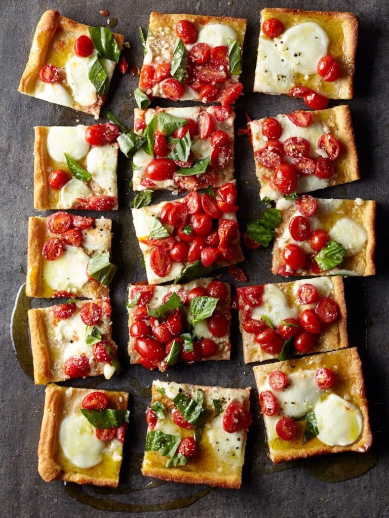 A top view of a sliced in squares cheesy tomato pizza