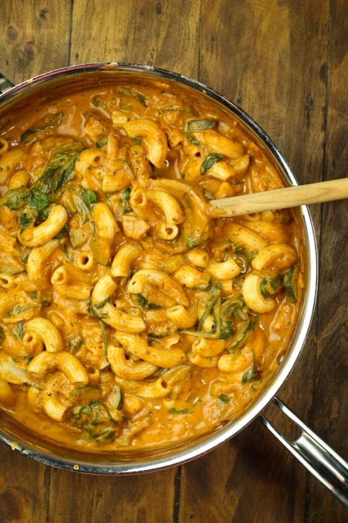 A top view of a vegan pasta mixed in sauce inside a pan with a ladle