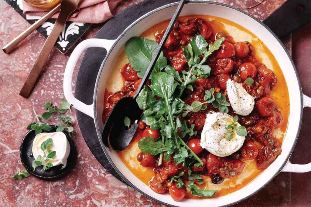 A top view of a vegetable italian soupy broth in a pot topped with burratta and cherry tomaotes