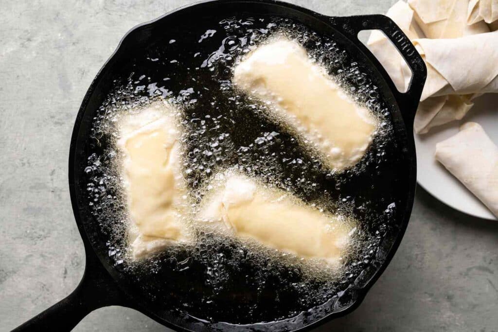 A top view of three egg rolls being fried