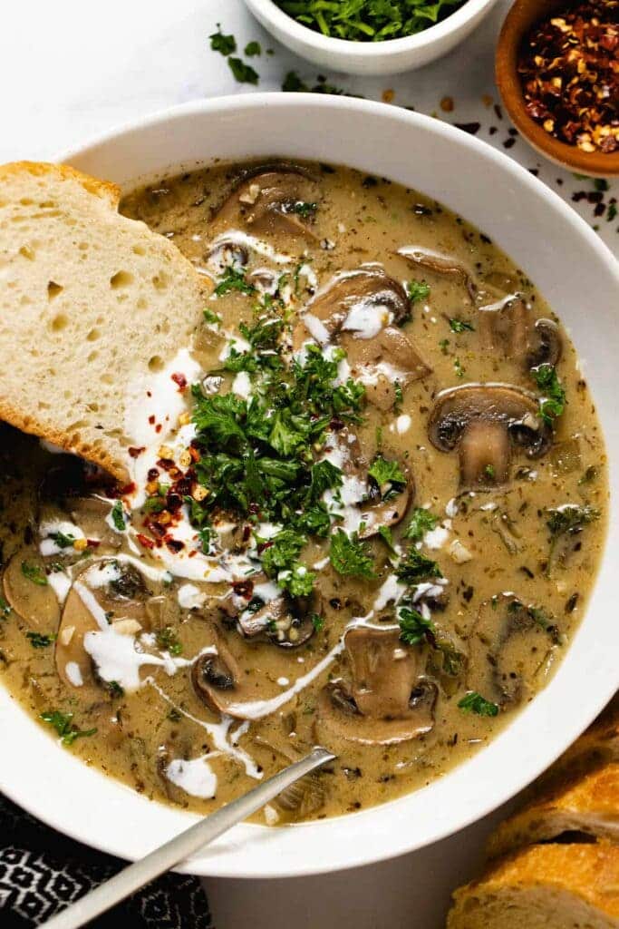 A top view of vegetarian mushroom soup served in a bowl with cream topping served with bread