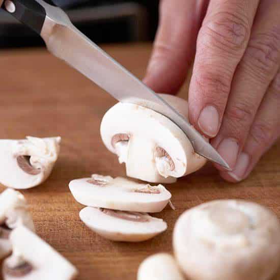 A view of a mushroom being sliced on the cutting board