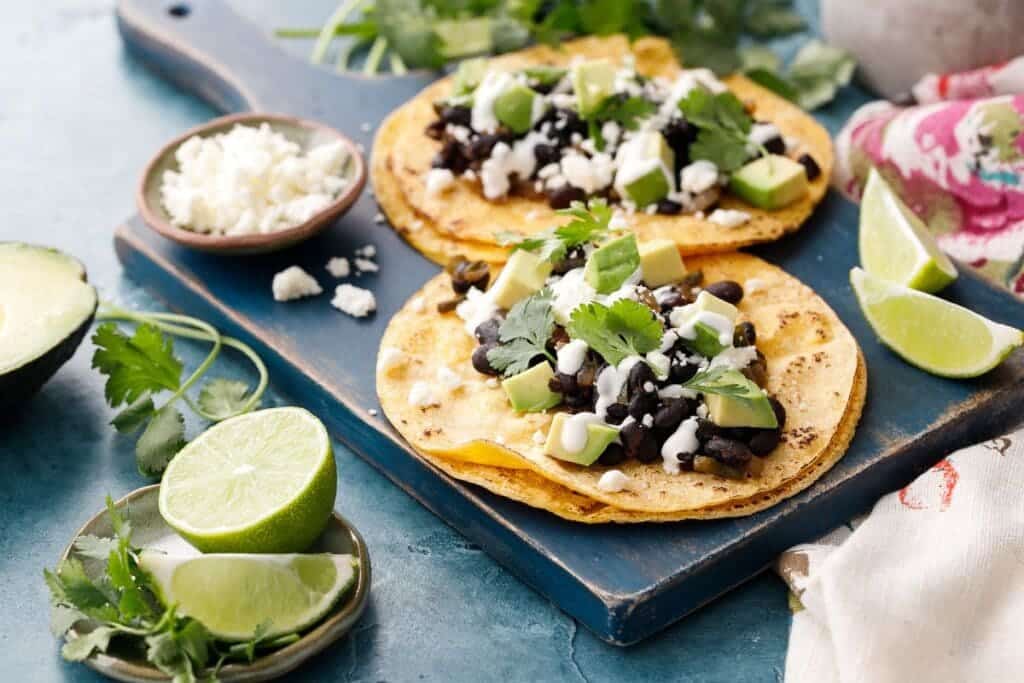 A view of black bean tacos with cream and cilantro on top and lemons on the side