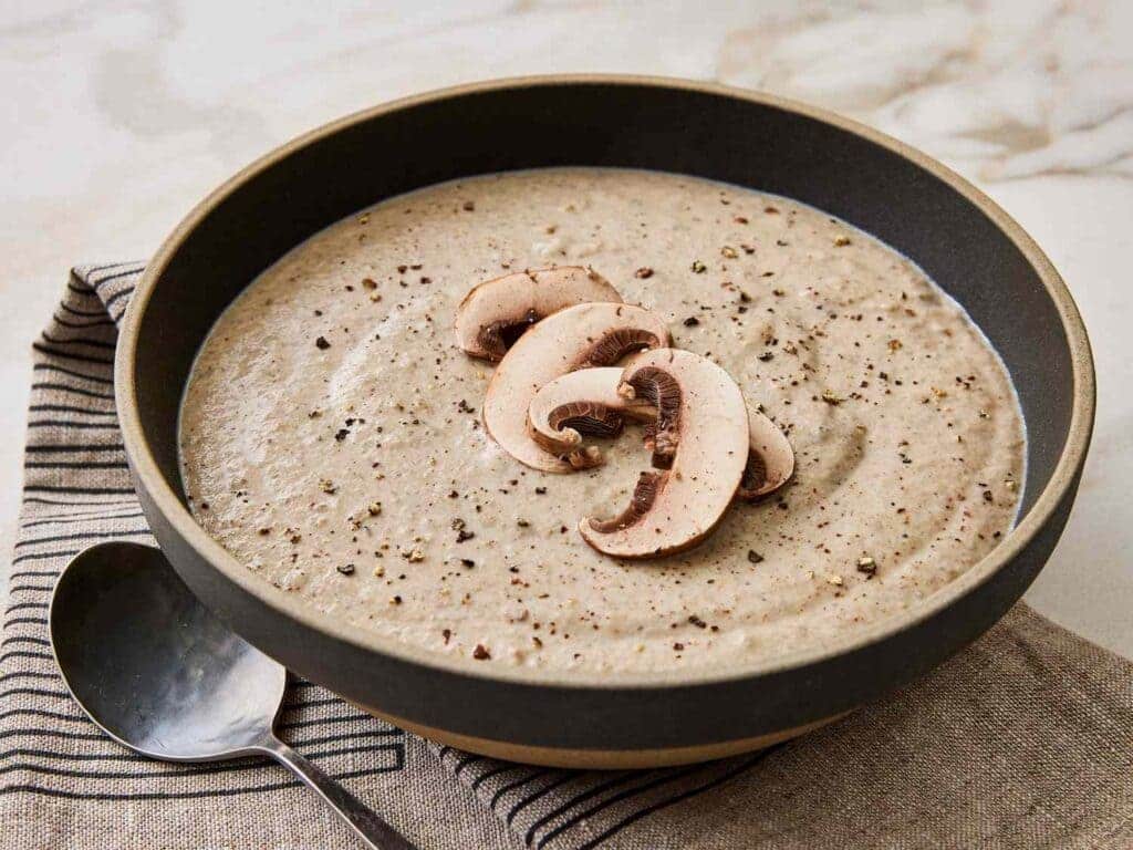 A view of cream of mushroom soup dished out in a bowl alongside a spoon