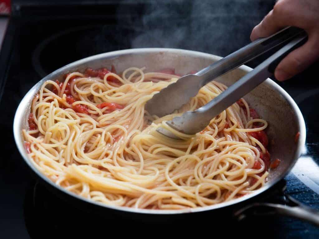 A view of mixing pasta in veggie sauce in a hot pan