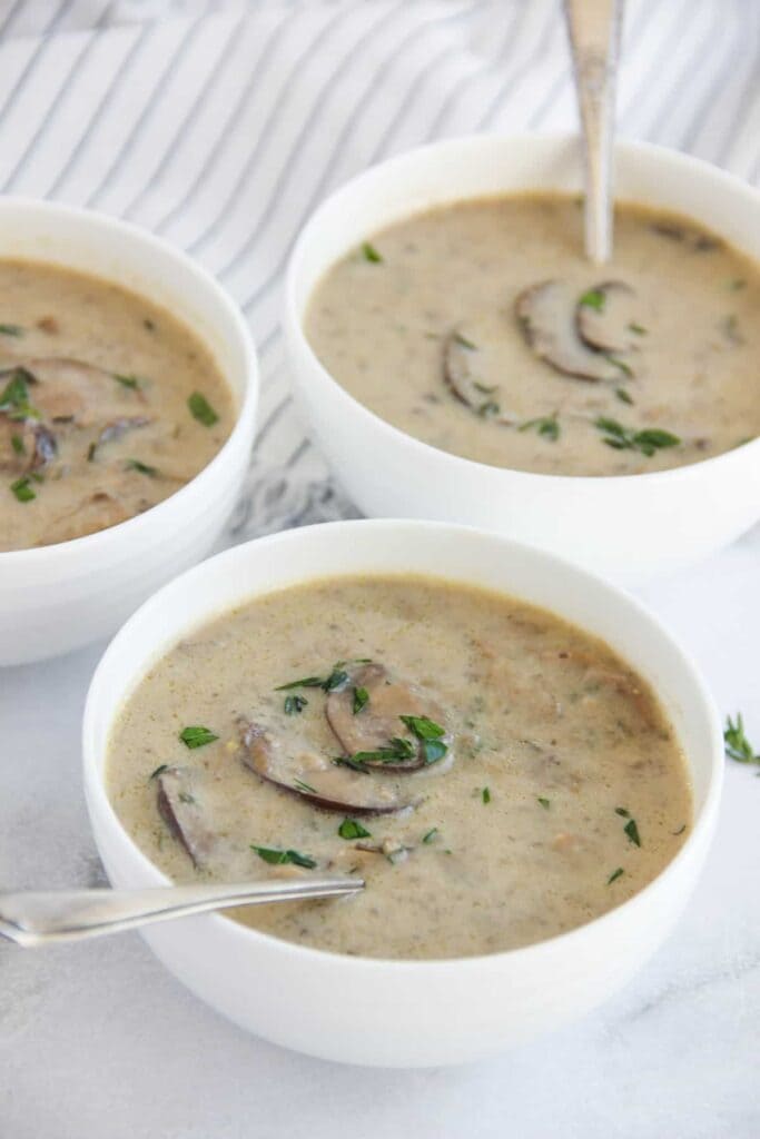 A view of three white mushroom soup bowls with spoons inside