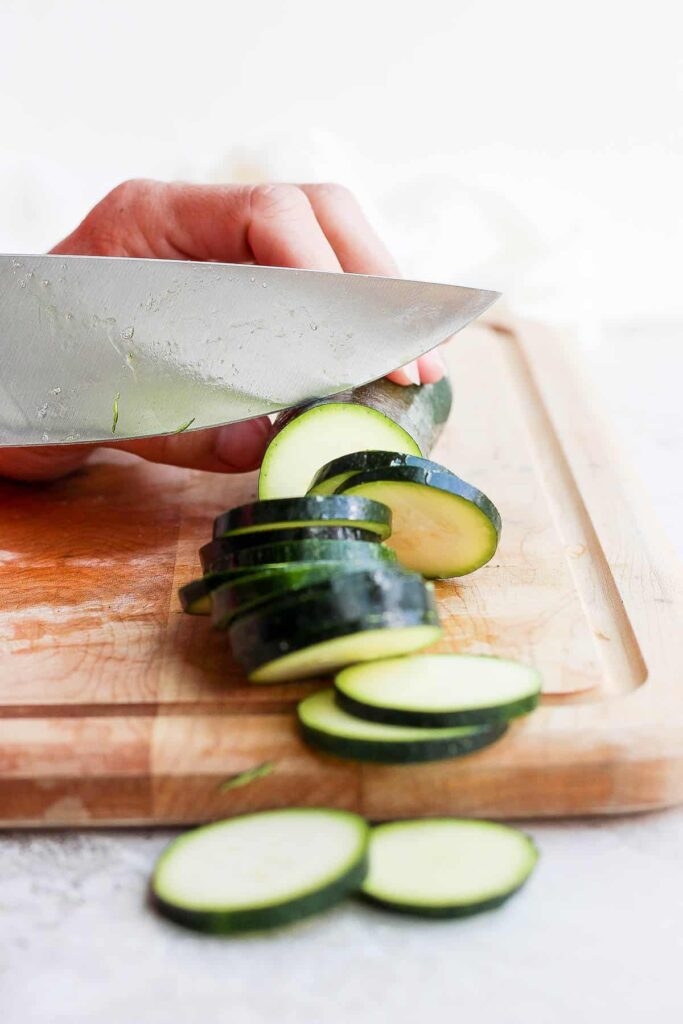 A view of zucchini being sliced with a knife on a board