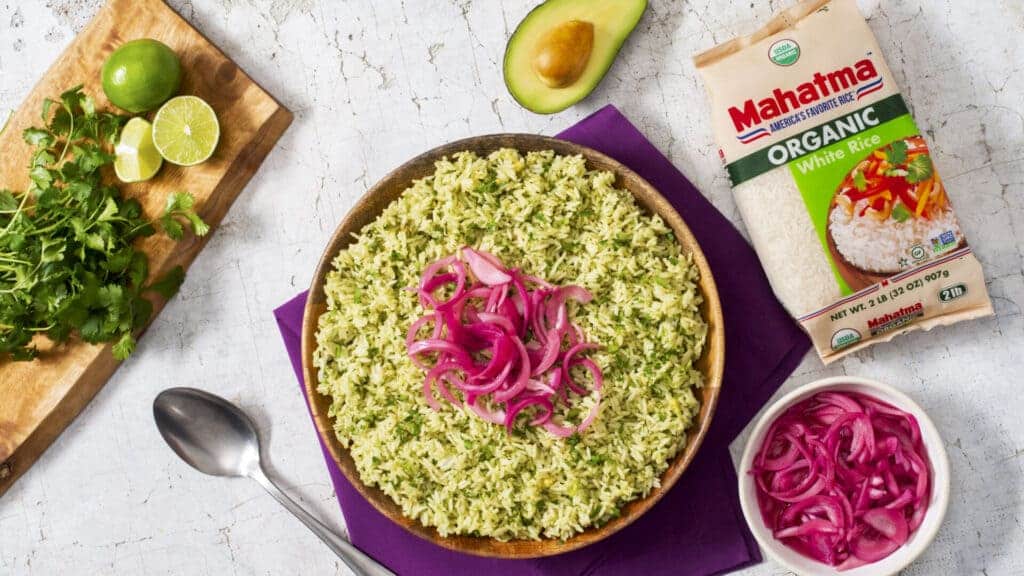 a bowl full of avacado and lime mexican rice garnish with fresh onion along with lime and cilantro on the chopping board