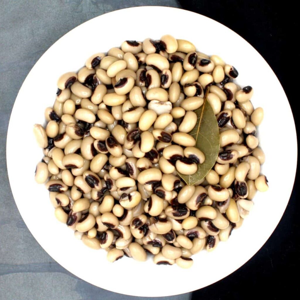 A top view of black eyed peas in a white bowl with a bay leaf in it