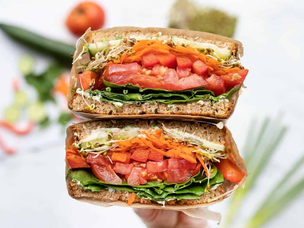 A view of a half sliced sandwich with wheat bread and filling of tomatoes