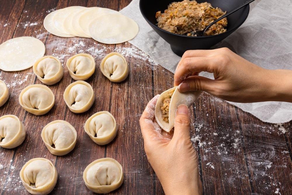 A view of a hand wrapping up dumplings with fillings