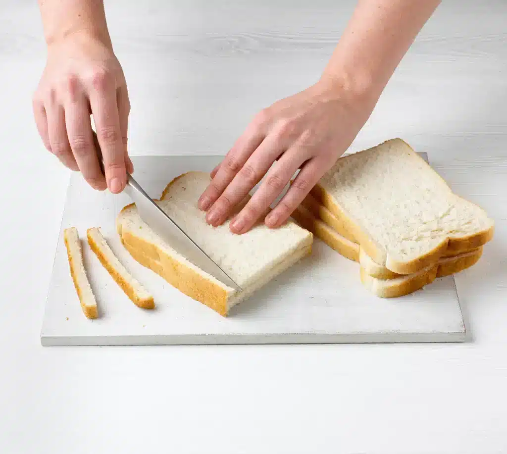 A view of a person cutting a sandwich crust with a knife to prepare it