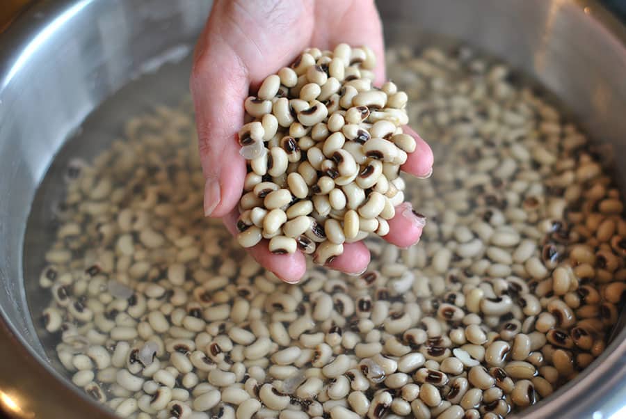 A view of a person holding a handful of sokaed black eyes beans in water