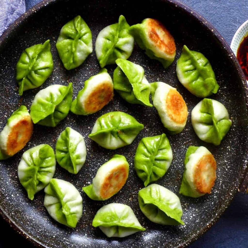 A view of vegetarian dumplings inside a pan with green sauce on them