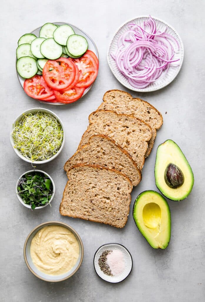 An overhead view of ingredients of a sandwich with wheat bread tomatoes onions avocado and cream cheese