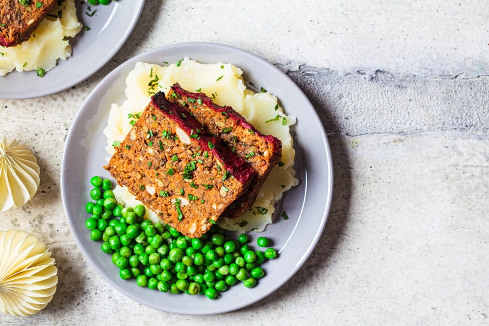 A top view of a veggie loaf dished out with mashed potatoes and some peas