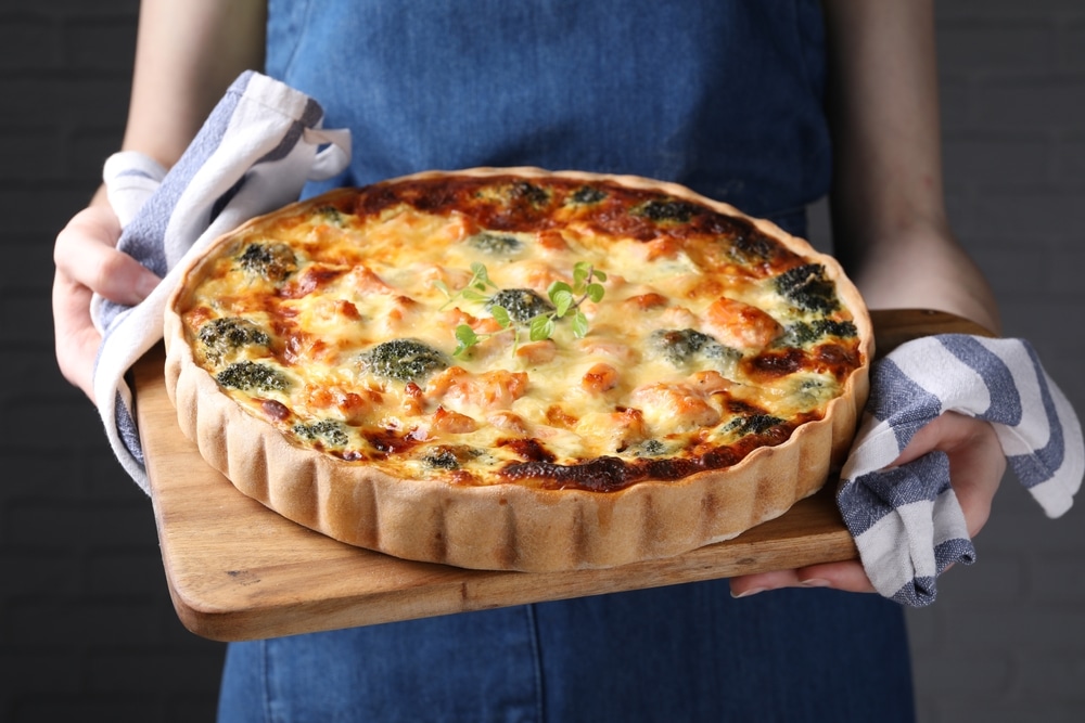 A view of a person holding a baked quiche inside a tray