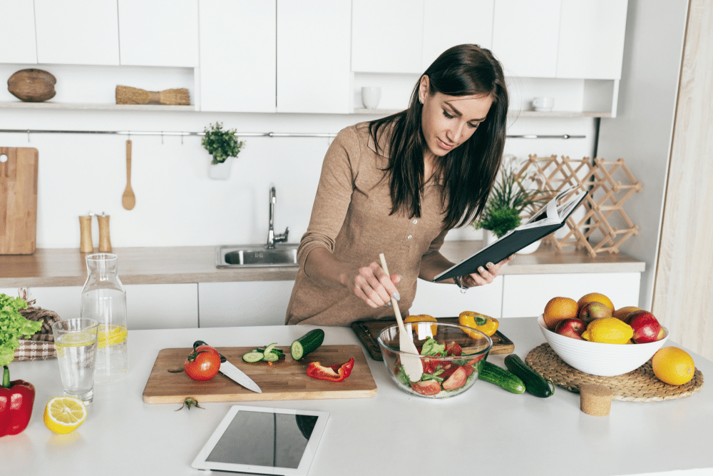 A view of a lady making a vegan salad with a cookbook in her hand