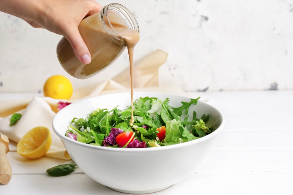 A view of a hand pouring dressing on a salad